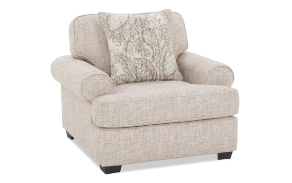 Beige fabric armchair with rolled arms, cushioned seat, and decorative patterned throw pillow, ideal for living room seating.