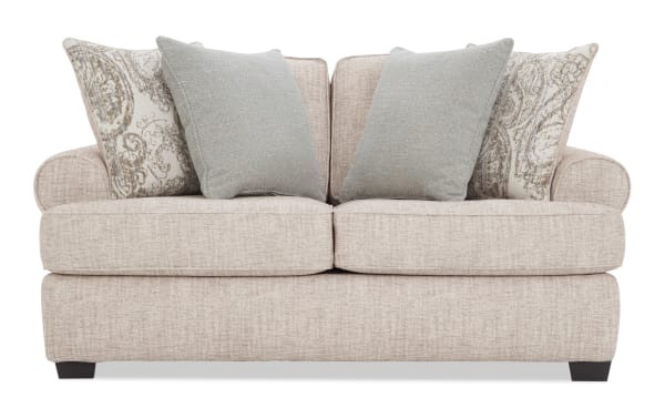 Beige fabric loveseat with rolled arms, featuring two solid light gray and two patterned beige-blue throw pillows, ideal for cozy living rooms.