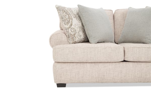 Beige fabric sofa with rolled arm, featuring three cushions—two solid light blue and one patterned in beige and blue tones—on dark wooden legs.