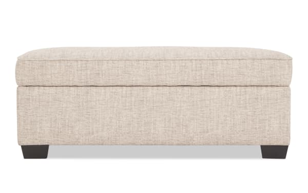 Beige fabric upholstered rectangular storage ottoman with cushioned top and dark wooden legs, suitable for living room seating and storage.