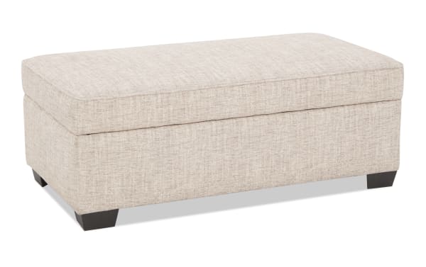 Rectangular beige fabric storage ottoman with cushioned top and dark wooden legs, suitable for living room seating and storage.
