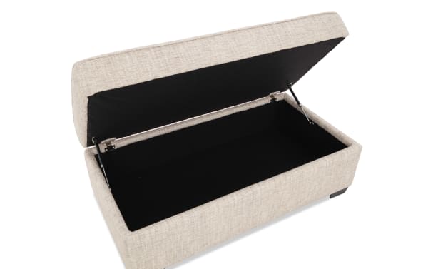 Beige fabric storage ottoman with hinged lid open, revealing spacious black interior for organizing household items.