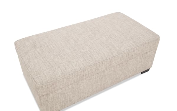 Rectangular beige fabric upholstered ottoman with subtle textured pattern and low black feet, suitable for living room seating or storage.