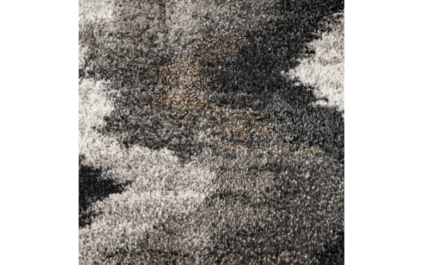 Close-up of a textured shaggy area rug with a mix of gray, black, beige, and brown tones, featuring a mottled abstract pattern.