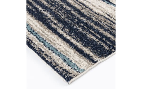 Close-up of a textured area rug corner with a striped pattern in navy blue, beige, and light teal, featuring a soft, plush pile and neatly finished edges.