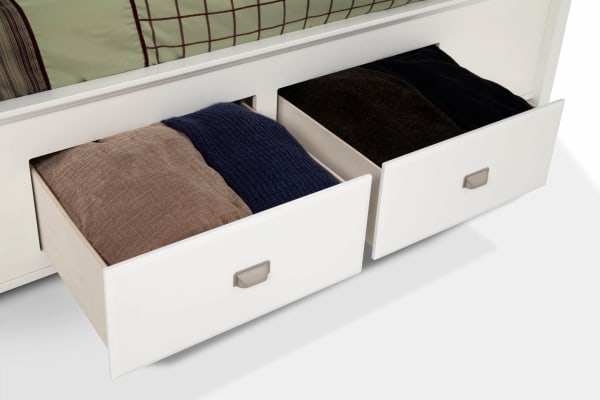 Two open white drawers with brushed metal handles under a Spencer Full White Storage Platform Bed, showing folded brown and navy knit blankets inside. The transitional style bed features hardwood solids, MDF, plywood, and poplar solids construction for durable bedroom storage.