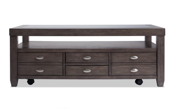Prestige Gray Storage Coffee Table from Prestige Occasional collection, transitional style with tempered glass top, solid acacia wood, metal oval handles, dual-sided storage drawers, open shelf, removable trays, and casters for easy mobility.