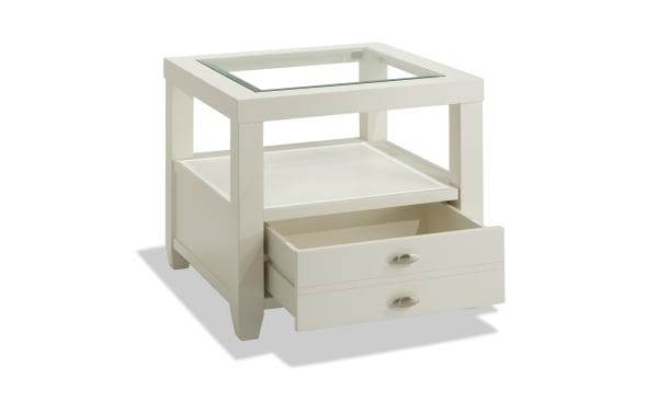 Prestige White Storage End Table from Prestige Occasional, transitional style with solid acacia, MDF, tempered glass top, beveled edge, open shelf, and drawer with oval metal handles.