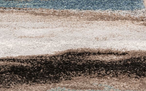 Soft textured area rug with horizontal stripes in blue, beige, brown, and black tones, featuring a plush pile and blended color gradient.