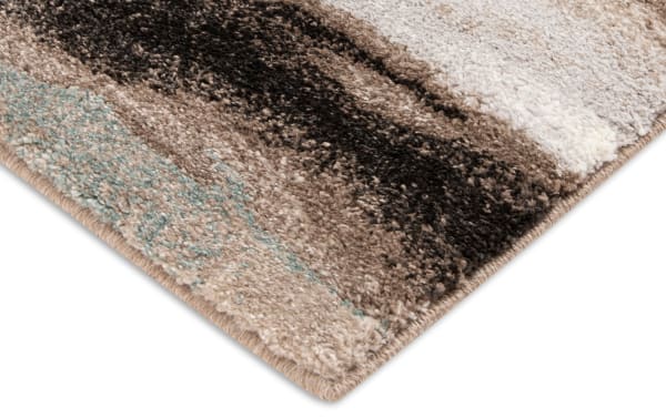 Corner close-up of a soft, plush area rug with a striped pattern in beige, brown, black, and light blue tones, featuring a thick pile and neatly finished edges.