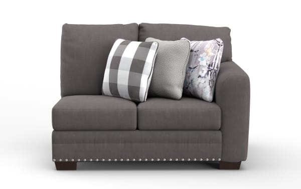 Gray fabric loveseat with three decorative pillows featuring checkered, houndstooth, and abstract patterns, accented with silver nailhead trim.