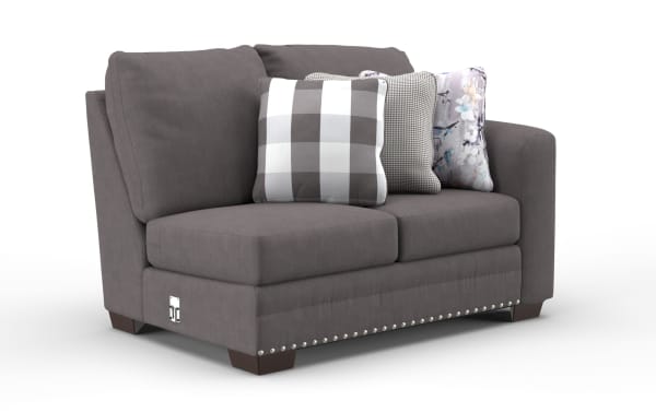 Gray fabric loveseat sofa with three decorative pillows in checkered, houndstooth, and floral patterns, featuring nailhead trim and wooden legs.