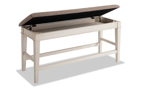 Montana White & Beige Upholstered Counter Height Storage Dining Bench with rustic white rubberwood frame, beige polyester fabric seat, and memory foam cushion. Features lift-top storage and sturdy MDF, plywood, and oak veneer construction. Perfect for rustic dining rooms needing functional seating and hidden storage.