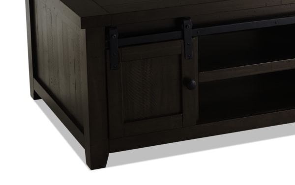 Rustic Montana Brown Storage Coffee Table from Montana Entertainment & Occasional collection, made of pine solids and plywood, featuring dark brown finish, gliding barn door with black metal hardware, storage shelves, and tapered legs.