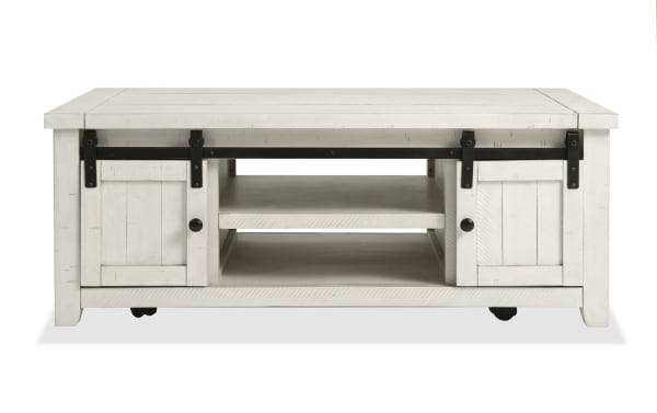 Rustic Montana White Storage Coffee Table from Montana Entertainment & Occasional collection, made of pine solids and plywood, with white finish, gliding barn doors, black metal hardware, open shelving, and casters for easy mobility.