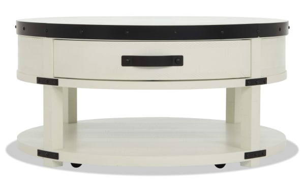 Round white wooden coffee table with black metal accents, a single drawer with black handle, and a lower shelf for storage.