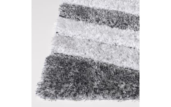 Corner view of a plush, shaggy area rug with thick, soft fibers in alternating gray and white stripes, ideal for cozy home decor.