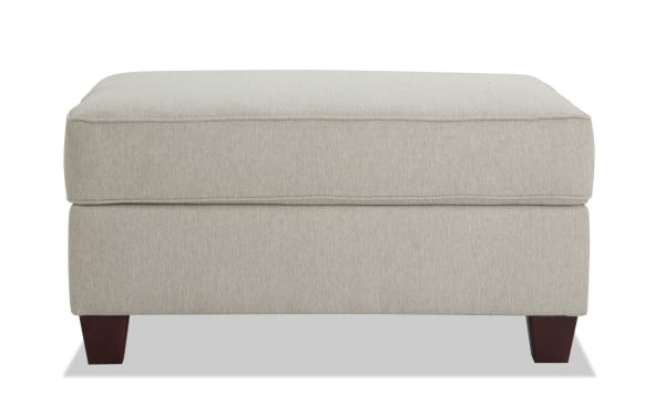 Beige Laurel Storage Ottoman with plush Bob-O-Pedic memory foam seat, transitional style, polyester fabric upholstery, and tapered dark wood legs.