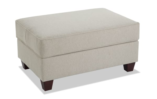 Beige Laurel Storage Ottoman in transitional style with plush Bob-O-Pedic memory foam seating, polyester fabric upholstery, and dark wooden legs.