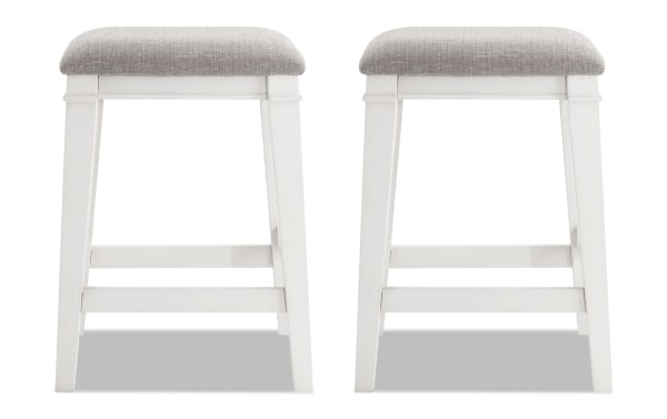 Set of 2 Montana White & Beige Backless Upholstered Counter Height Stools with beige polyester fabric seats, rustic rubberwood frames, and memory foam cushions.