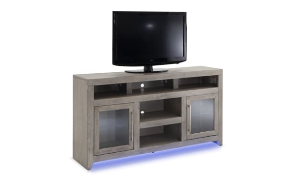 Cosmopolitan 65'' gray MDF and acacia veneer TV stand with glass doors, LED lighting, soundbar shelf, and silver hardware in contemporary style.