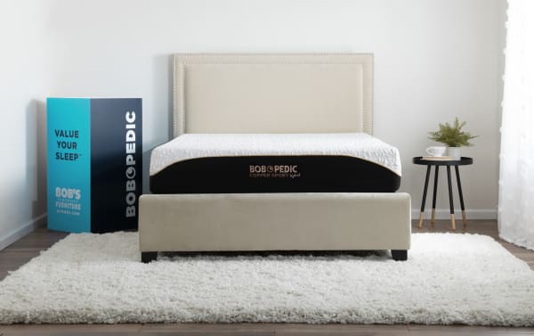 King-sized Copper Sport Hybrid 11.5" Plush Mattress by Bob-O-Pedic with cool-touch copper thread cover, layered memory foam, and beige upholstered bed frame.