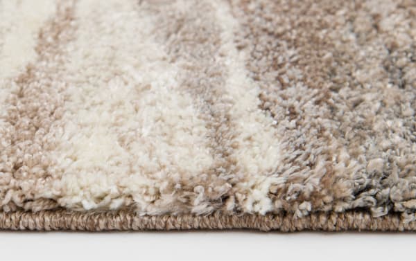 Close-up of a beige and cream striped shaggy area rug with thick, soft pile and tightly woven edge, showcasing texture and color details.