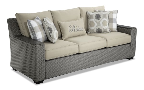 Cottage Chic Beige Wicker Outdoor Sofa with beige polyester cushions, rust-proof aluminum frame, wicker weave, and decorative floral and plaid accent pillows.