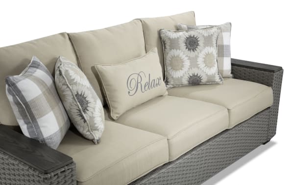 Cottage Chic Beige Wicker Outdoor Sofa with beige polyester cushions, rust-proof aluminum frame, plush Bob-O-Pedic foam, and floral & plaid accent pillows.