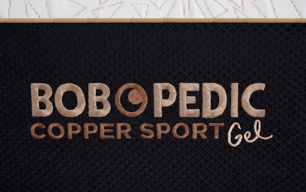 Bob-O-Pedic Copper Sport Gel mattress label embroidered in copper and beige thread on black textured fabric, highlighting the Copper Sport collection.