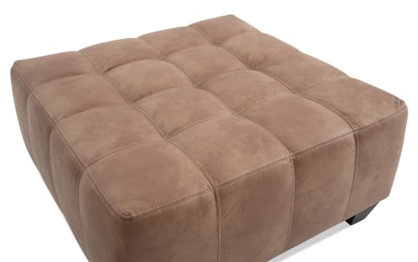 Transitional Sierra Cognac Ottoman in brown polyester and polyurethane fabric with tufted design, memory foam padding, and sturdy black legs.