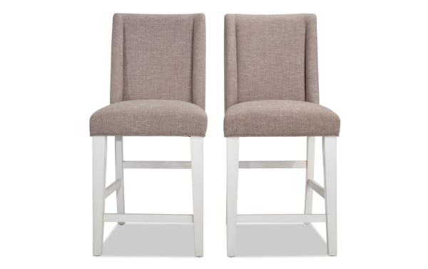 Set of 2 Montana Dining rustic counter height stools with beige polyester fabric upholstery, solid back, and white rubberwood legs, featuring memory foam seats.