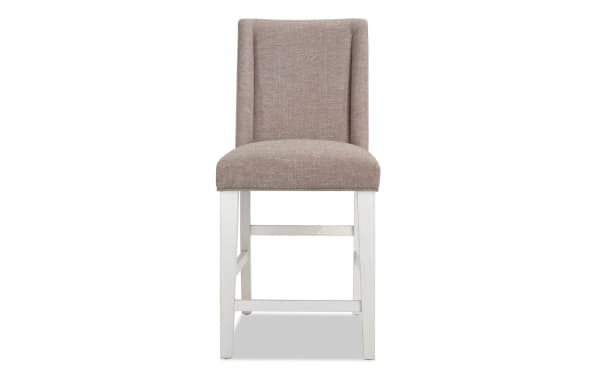 Rustic Montana Dining counter height stool with beige polyester fabric upholstery, solid back, memory foam seat, and white rubberwood legs.