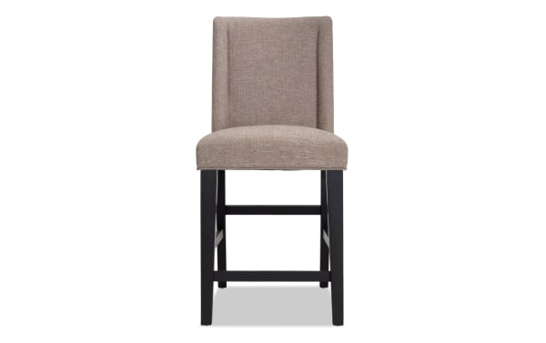Beige upholstered Montana Dining counter height stool with solid back, black rubberwood legs, rustic style, and memory foam seat for comfort.