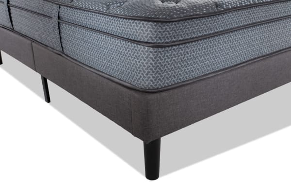 Corner view of Synergy 11'' Full Plush Universal Mattress Set in gray-blue patterned fabric with dark gray upholstered foundation and black tapered legs, featuring plush cushioning and durable coil support for enhanced comfort and temperature regulation.