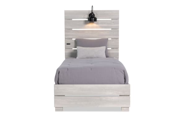 Foundry Twin White Storage Platform Bed with rustic whitewashed MDF and engineered wood grain, paneled slat headboard, built-in black lamps, and USB charging port.