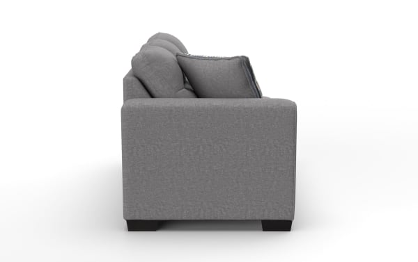 Modern gray fabric sofa side view showing cushioned armrest, plush back pillows, and dark wooden block legs for living room seating.