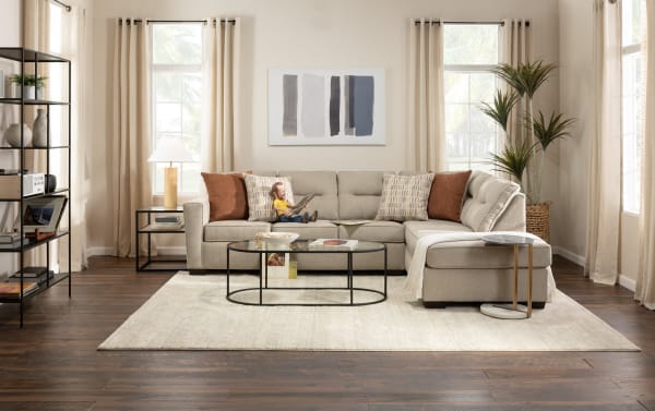 Dylan Slate 112" 2-piece right arm facing sleeper chaise sectional in gray polyester fabric with transitional style. Features four accent pillows and a glass coffee table on a light rug. Includes Cooling Bob-O-Pedic gel memory foam mattress for temperature-sensitive comfort.