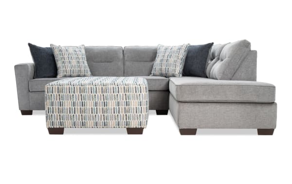 Dylan Slate 112" 2-piece right arm facing sleeper chaise sectional in gray polyester fabric with tufted back cushions, four accent pillows, and patterned ottoman. Transitional style with memory foam queen gel mattress for comfort and versatile seating.