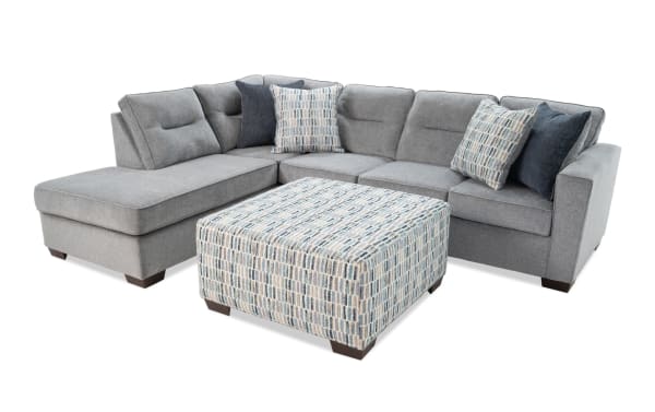 Dylan Slate 112" 2-piece left arm facing sleeper chaise sectional in gray polyester fabric with four accent pillows and patterned ottoman. Transitional style with queen gel memory foam mattress for comfort and overnight guests.
