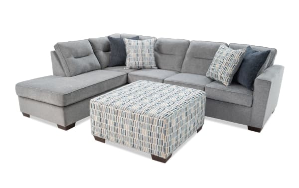Dylan Slate 112'' 2-piece left arm facing sleeper chaise sectional in gray polyester fabric with transitional style, four accent pillows, and patterned ottoman. Includes Cooling Bob-O-Pedic gel memory foam queen mattress with cooling fabric cover for temperature-regulated comfort.