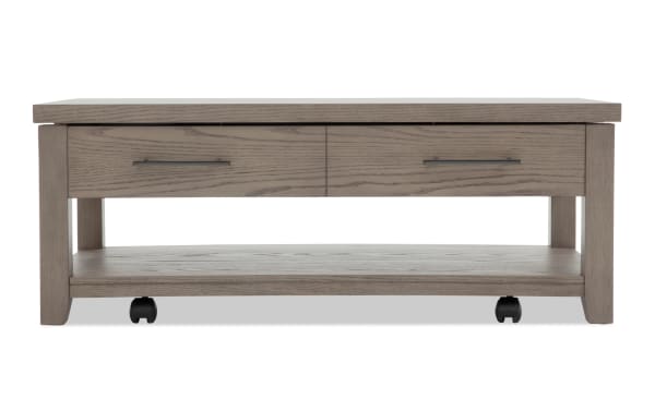 Rectangular gray wood coffee table with two drawers, metal handles, lower shelf, and caster wheels for mobility.