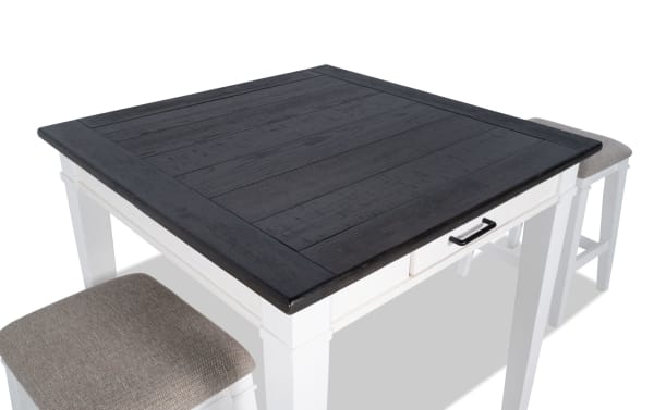 Montana 3 Piece Rustic Counter Height Dining Set with distressed black oak veneer top, white rubberwood base, and beige upholstered backless stools with memory foam.