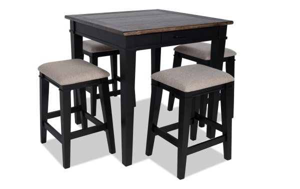 Montana 5 Piece Rustic Counter Height Dining Set with black rubberwood frame, beige polyester upholstered backless stools, oak veneer distressed tabletop, and built-in storage drawer.