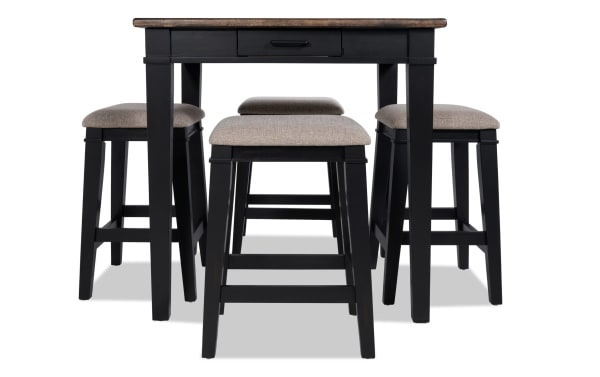 Montana 5 Piece Black & Beige Upholstered Counter Height Dining Set with rubberwood, oak veneer top, rustic style, fabric cushioned stools, and storage drawer.