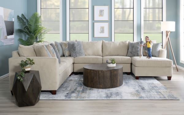 Beige Brynn sectional sofa with plush polyester fabric upholstery, transitional style, featuring multiple cushions, a round dark wood coffee table, and a patterned area rug.