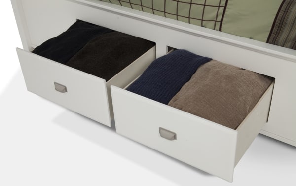 Two open white storage drawers from the Spencer 4 Piece Full White Storage Platform Bedroom Set, showing folded dark and neutral colored clothing inside. The transitional style drawers feature hardwood solids, MDF, plywood, poplar solids, and veneers, designed for organized clothing storage under a platform bed.