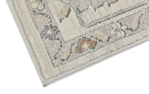Corner close-up of Clara 5' x 7' light gray oriental rug with a soft polyester fabric, featuring a neutral, calming floral border pattern.