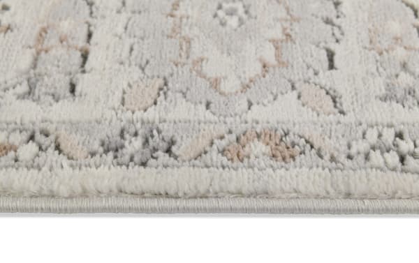 Close-up of the Clara 5' x 7' light gray oriental rug edge showing soft polyester fabric with a neutral, intricate oriental pattern and plush texture.