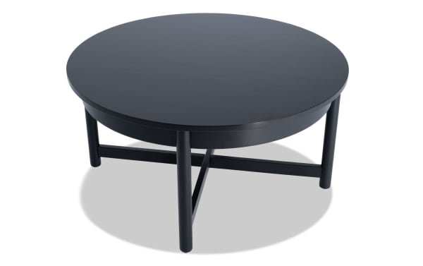 Bettie Black Round Coffee Table from Bettie Entertainment & Occasional collection, mid-century modern style, black wood with round top and slender legs.